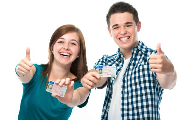 2 smiling teens holding their drivers licenses